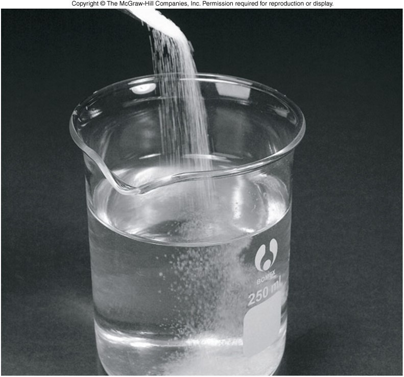 A photograph showing table salt, sodium chloride, being poured into a beaker of water.
